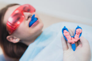 Patient undergoing a dental examination with protective eyewear, while a dental professional holds a dental impression tray filled with pink material, illustrating preventive dental care procedures.