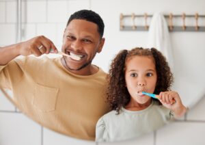 Father and daughter brushing teeth together, promoting oral hygiene and the importance of daily dental care.